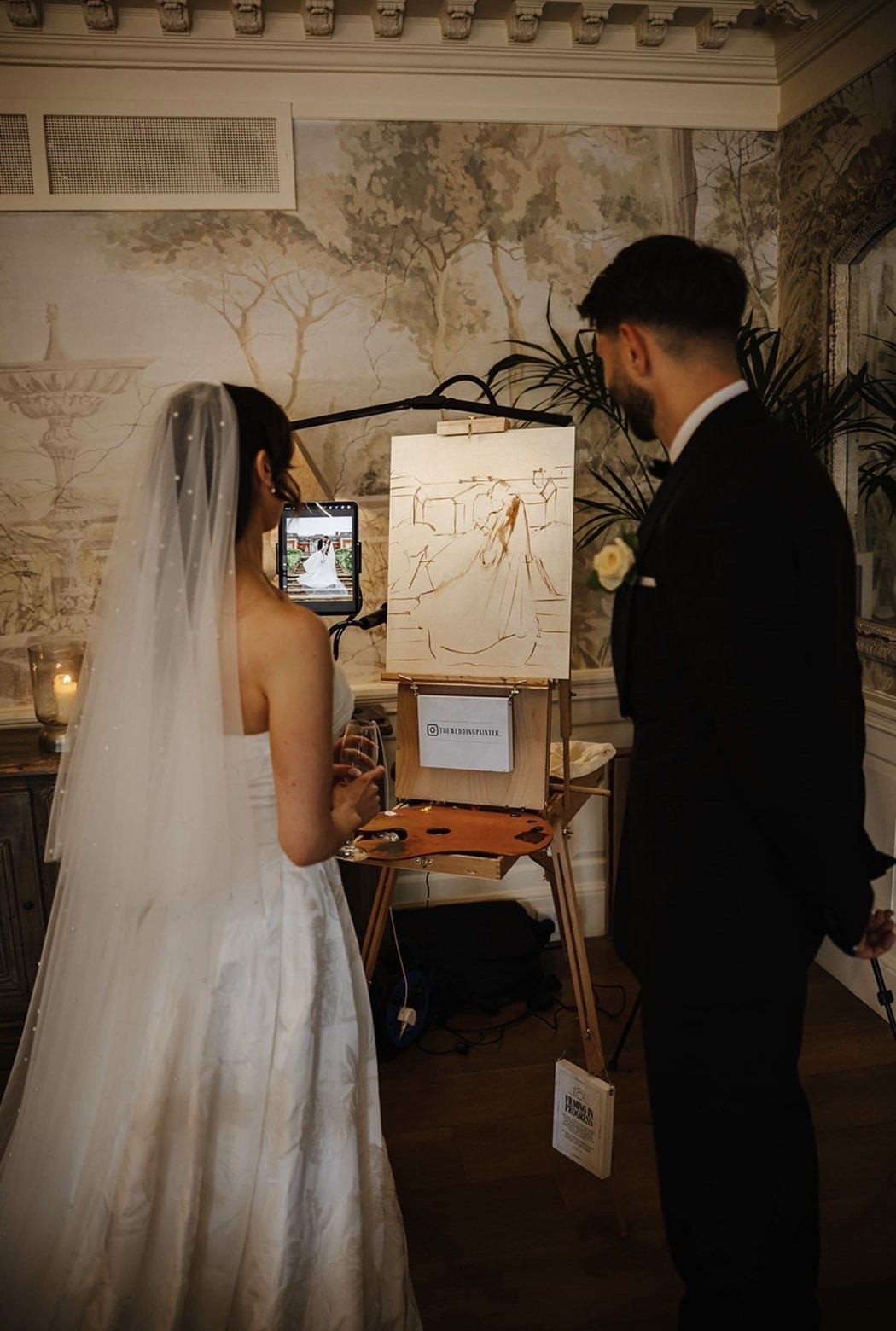 A bride and groom at the easel, watching their painting take shape during the reception