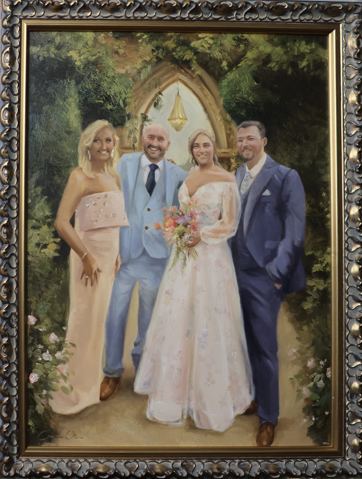 Ornately framed oil painting of a bride and groom with family beneath a stone archway hung with a lantern, framed by climbing roses